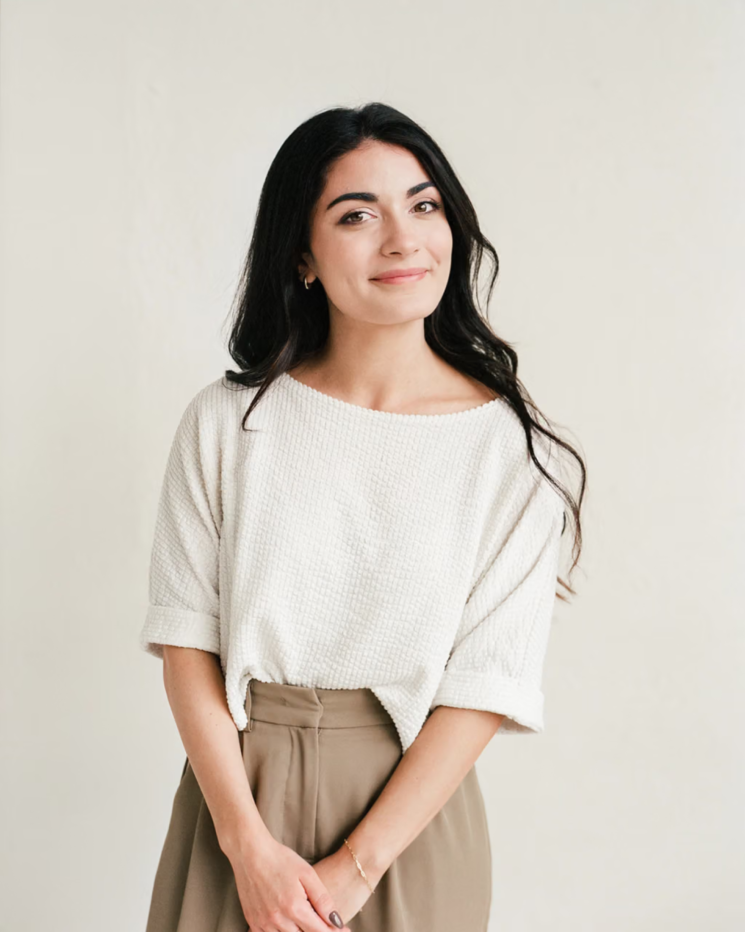 Angela Beausoleil smiles in a cream textured top with her dark hair down against a plain white backdrop.