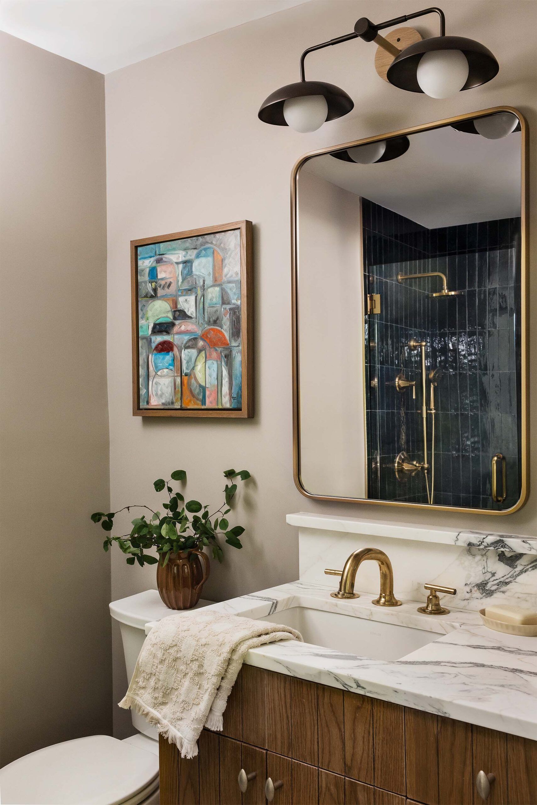 Bathroom vanity with a marble countertop, a brass faucet, brass and alabaster sconces, and a rounded brass-framed mirror.