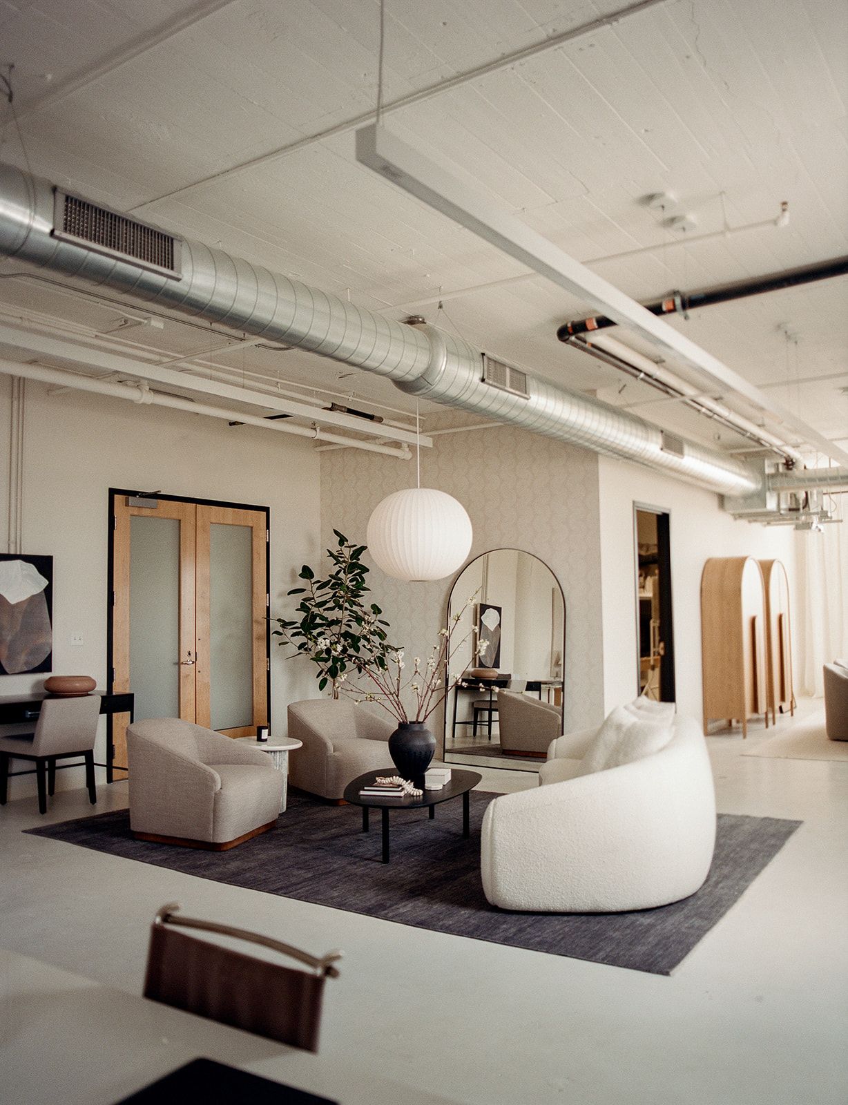 Lounge area with a white globe pendant, an arched mirror, wood louvered doors, abstract art, beige swivel chairs, and a charcoal rug.