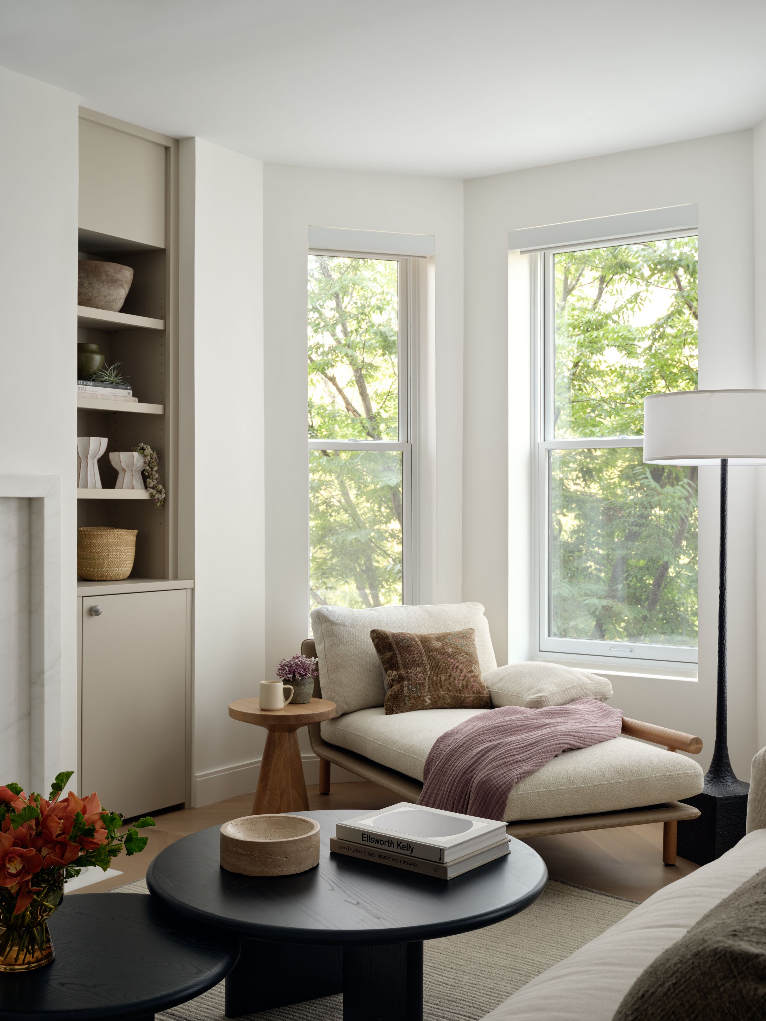 A living room reading nook with built-in shelving, a cushioned daybed chaise, bay windows, and a round black coffee table.