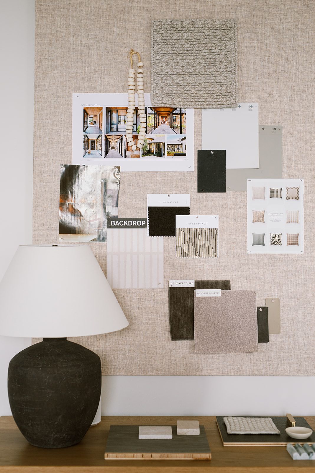 Mood board pinned with fabric swatches, a pillow sample sheet, and a wood bead tassel above a dark ceramic table lamp.