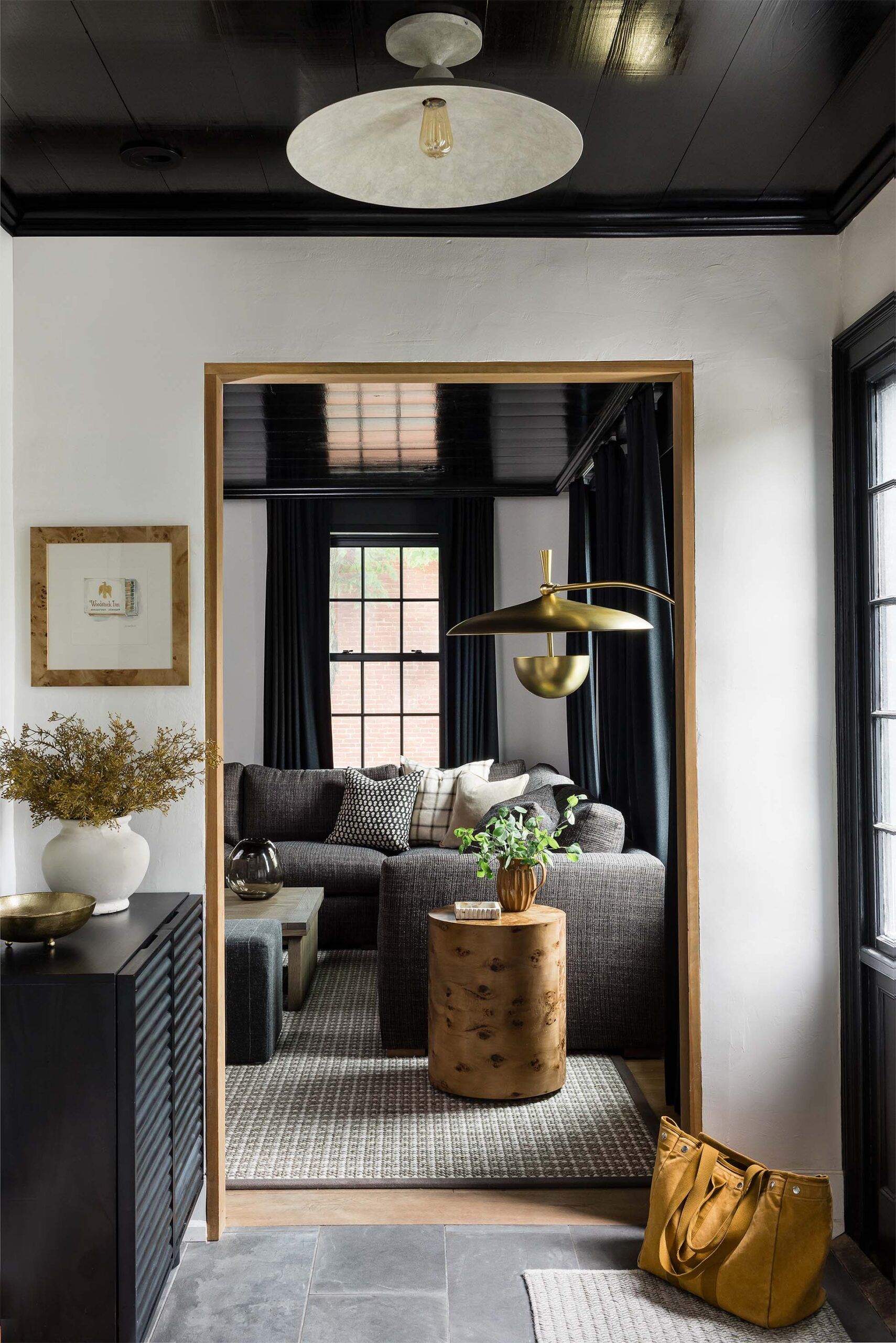 Entry with a black lacquered cabinet opens to a living room with a gray sectional sofa and a gold articulated pendant lamp.