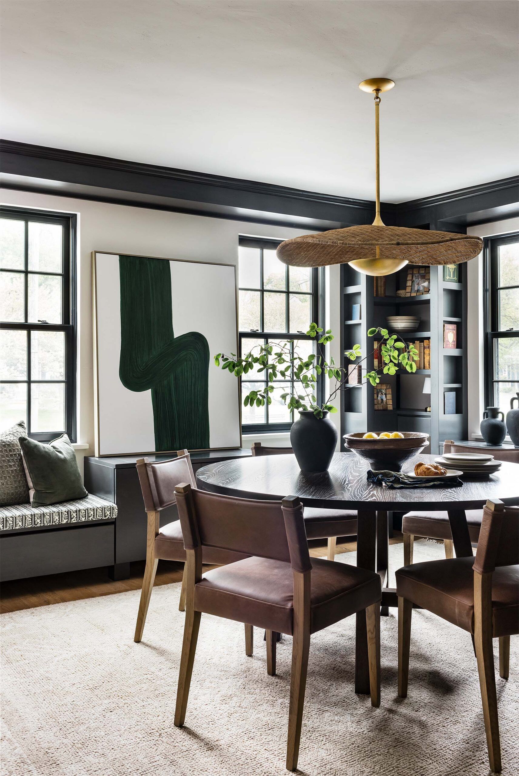 Dining room with a round dark wood table, leather chairs, a green abstract painting, and a built-in black bookshelf.