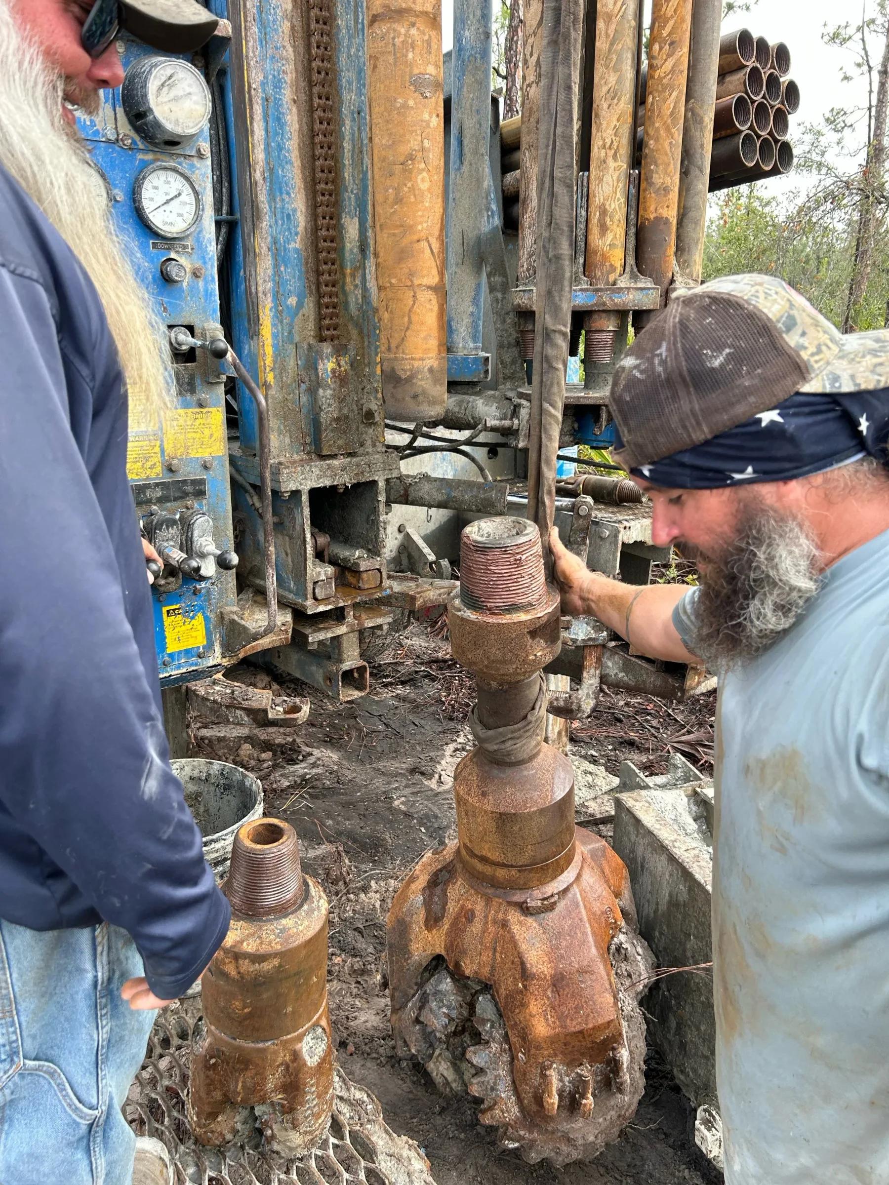 Crew member standing beside large drill bits at the rig