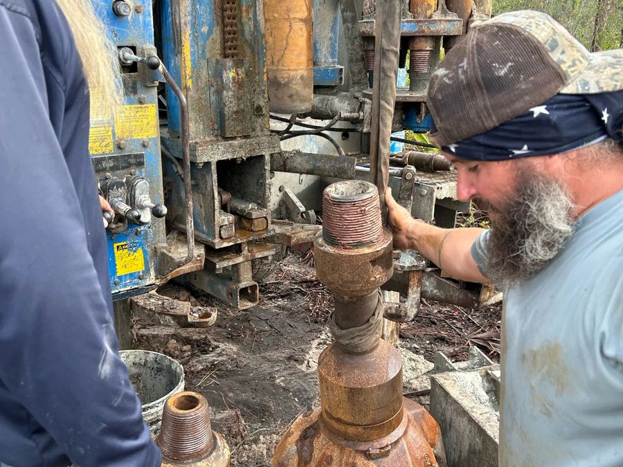 Crew member standing beside large drill bits at the rig