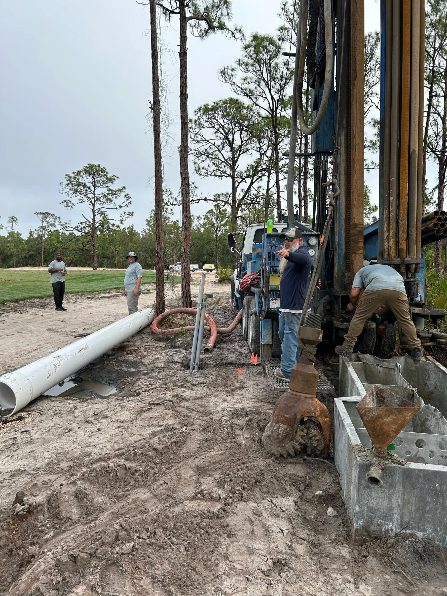 Crew drilling on an open site with lengths of white casing on the ground