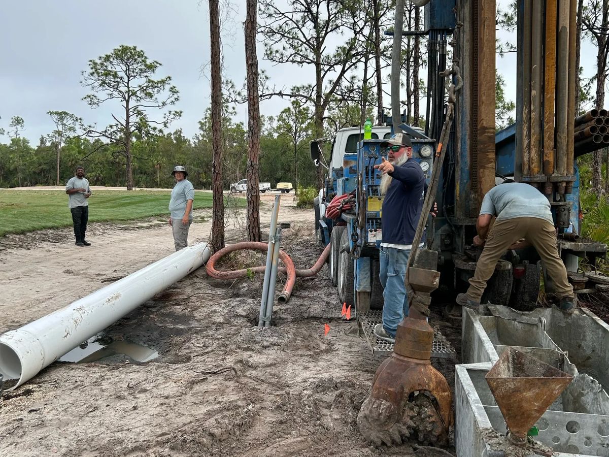 Crew drilling on an open site with lengths of white casing on the ground