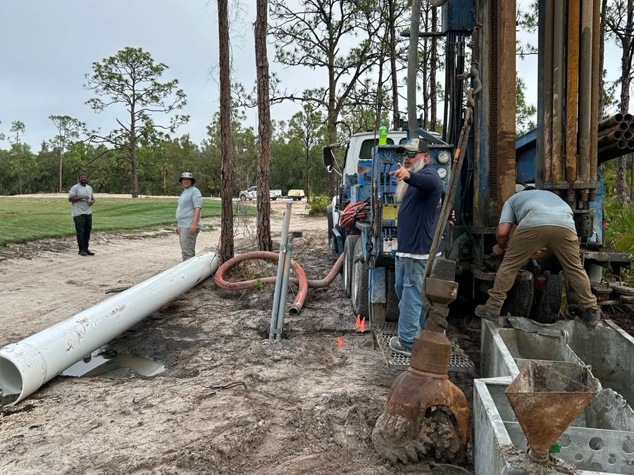 Crew drilling on an open site with lengths of white casing on the ground