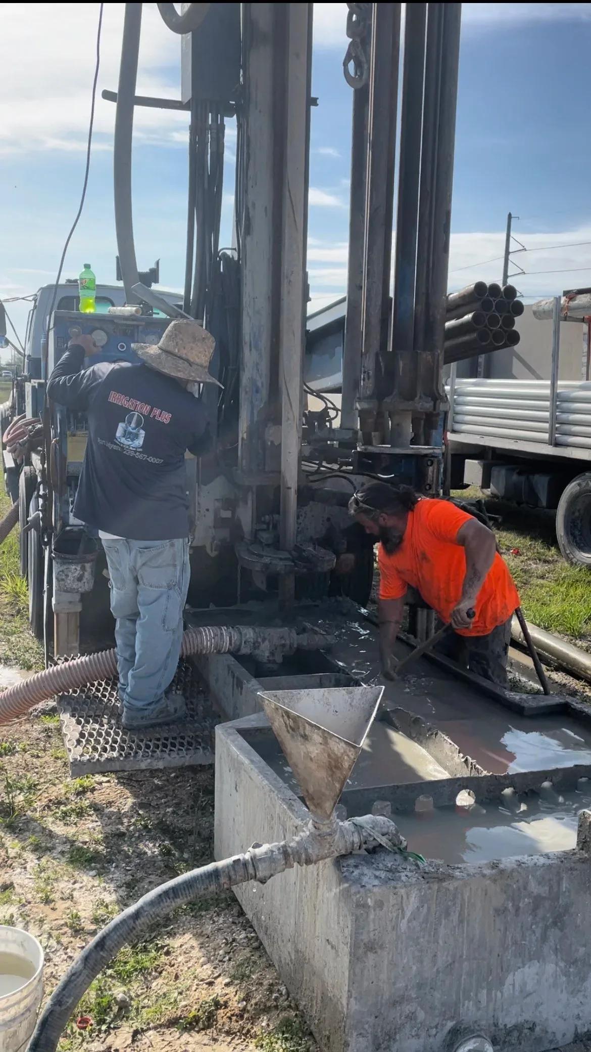 Two crew members working at the mud pit beside the drill rig