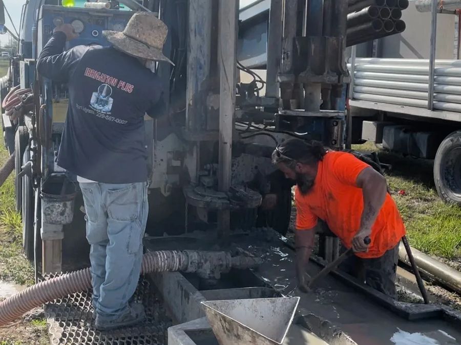Two crew members working at the mud pit beside the drill rig