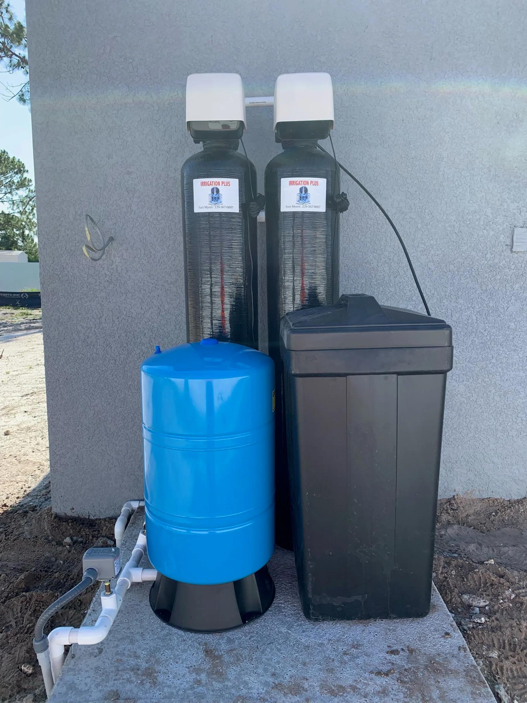 Two filtration tanks, a blue pressure tank and a brine tank installed beside a house
