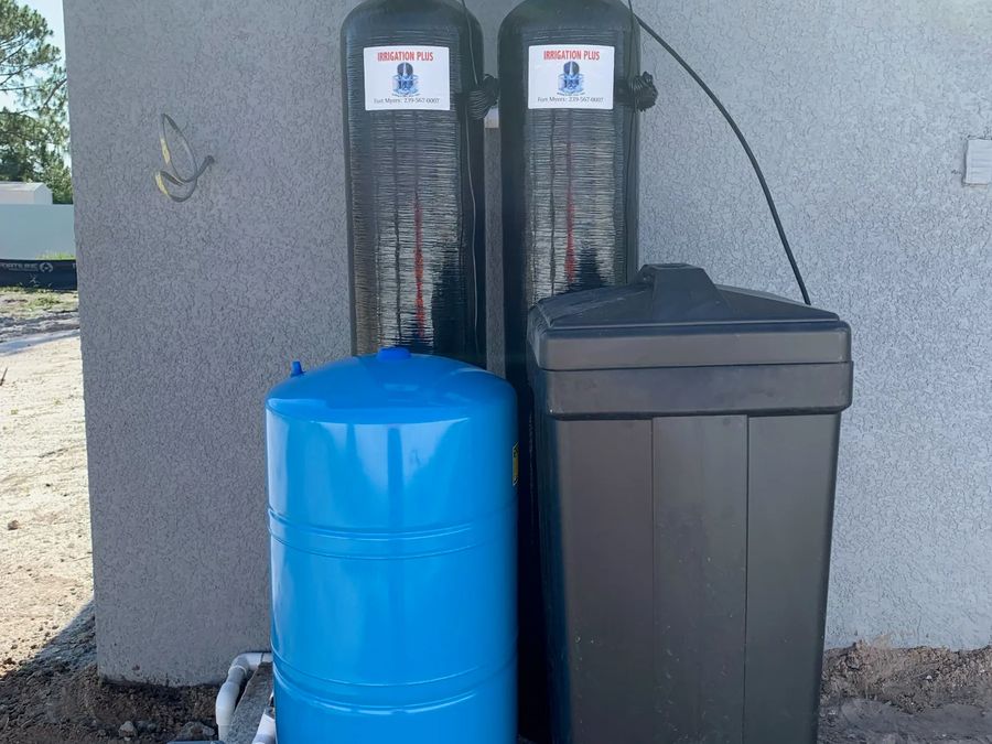 Two filtration tanks, a blue pressure tank and a brine tank installed beside a house