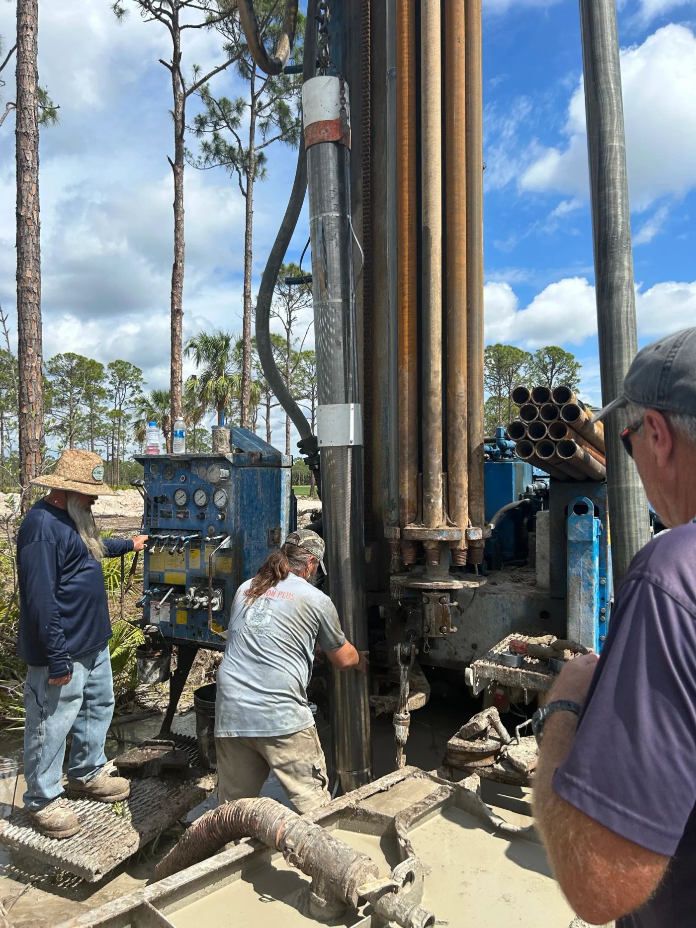 Three crew members at the drill rig controls with drill pipe racked overhead
