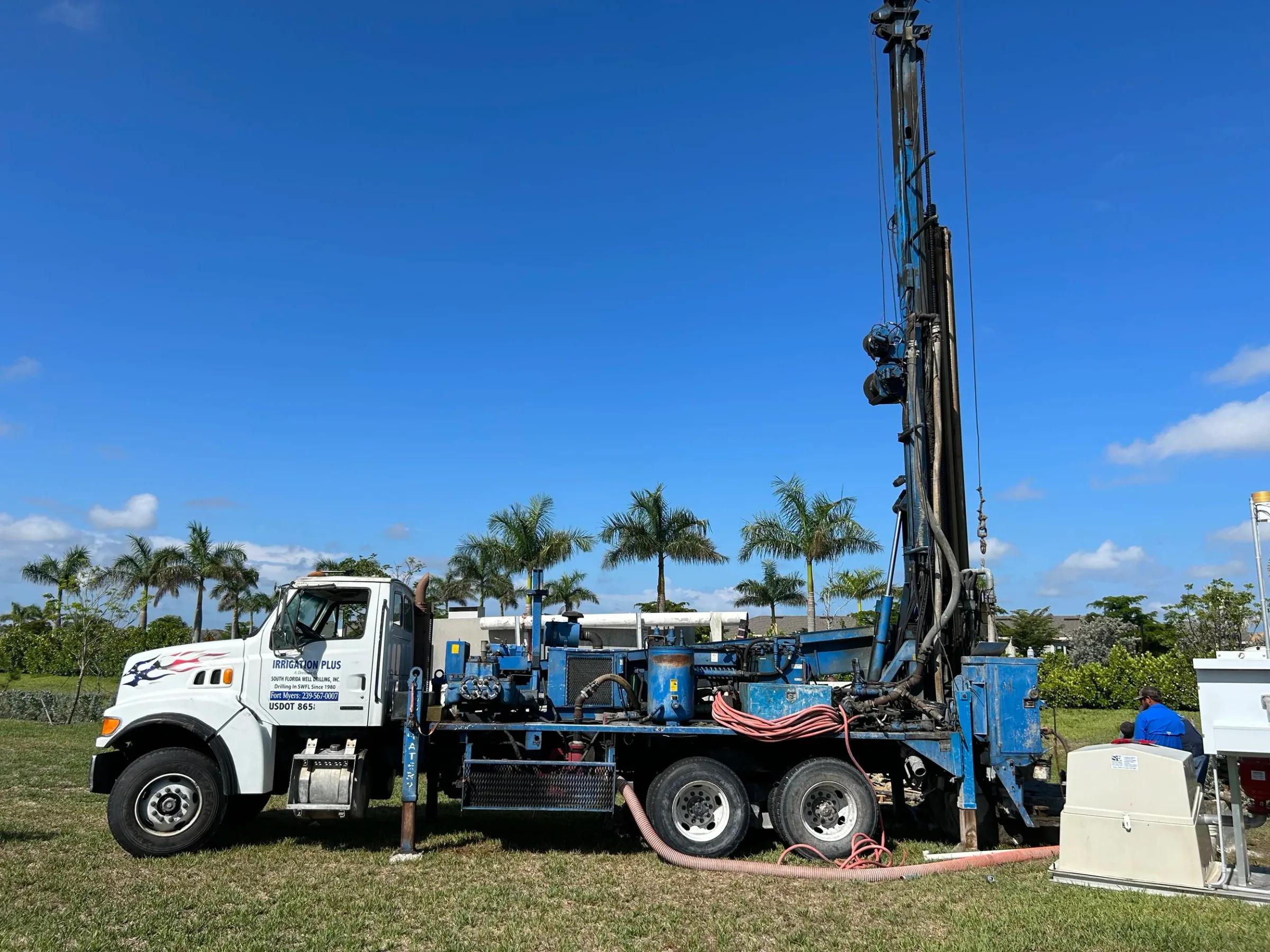 Irrigation Plus drill rig truck parked on a grass lot with palm trees behind it