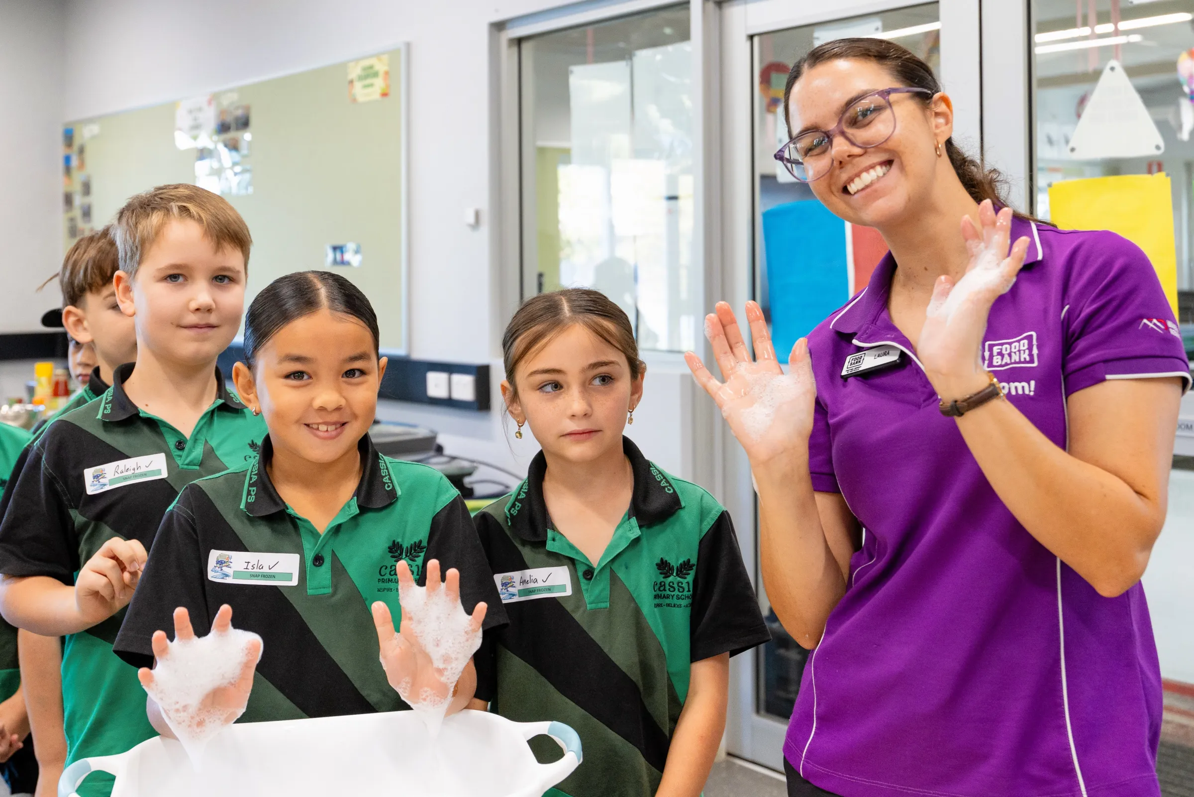 3 school kids and a foodbank educator smiling washing their hands