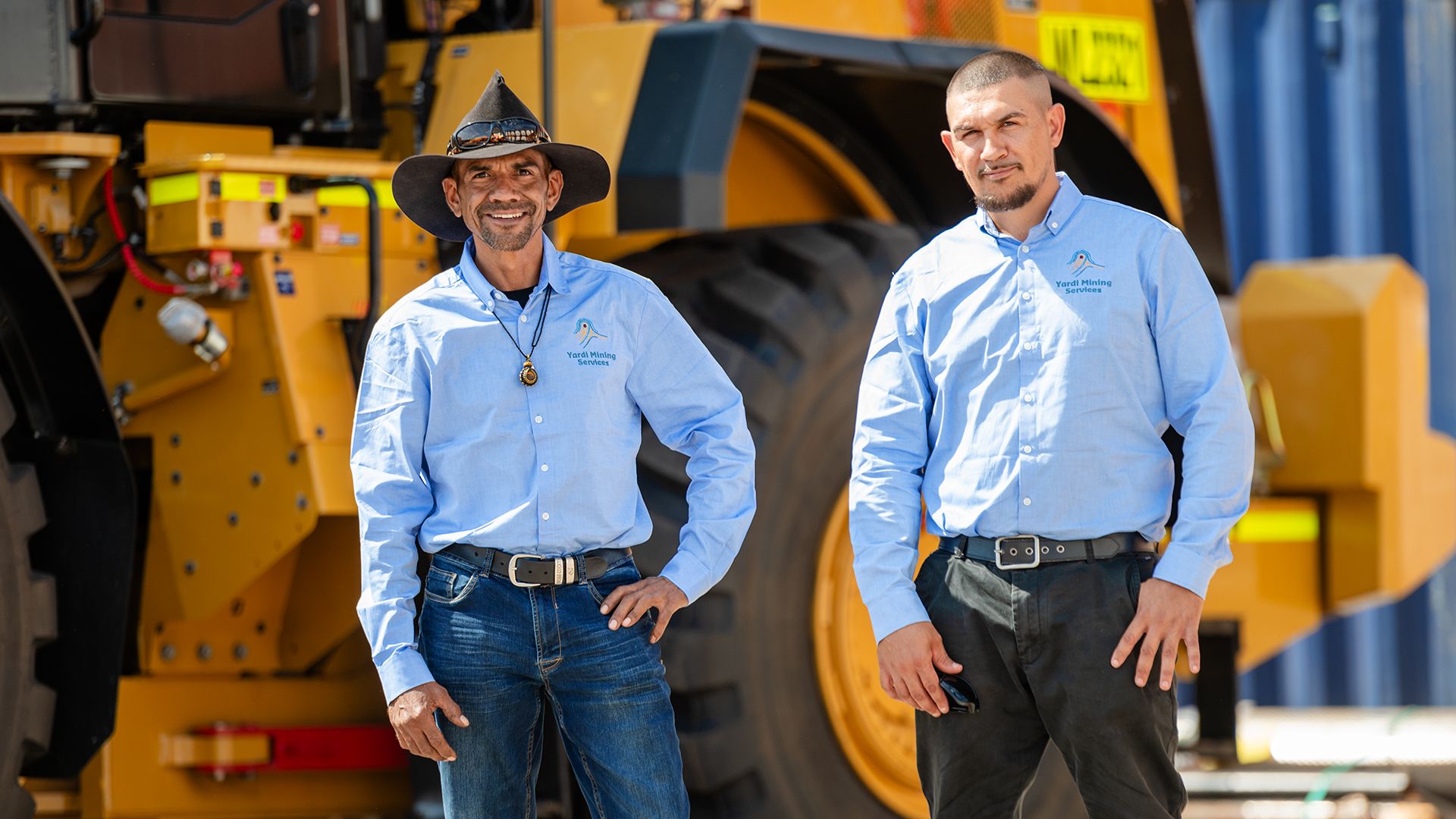 Two Indigenous men standing in front of mining machinery