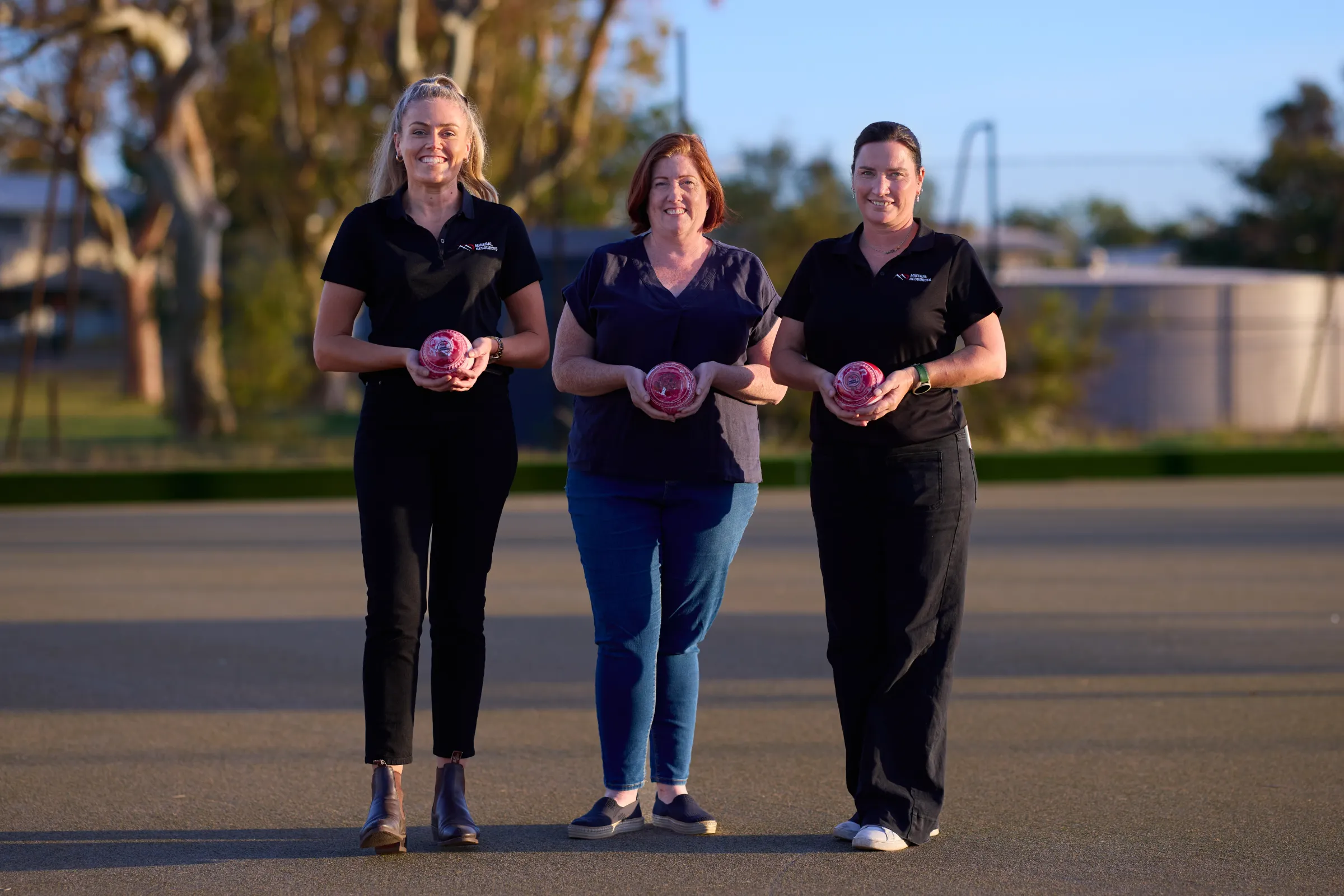 three women standing holding a lawn bowl