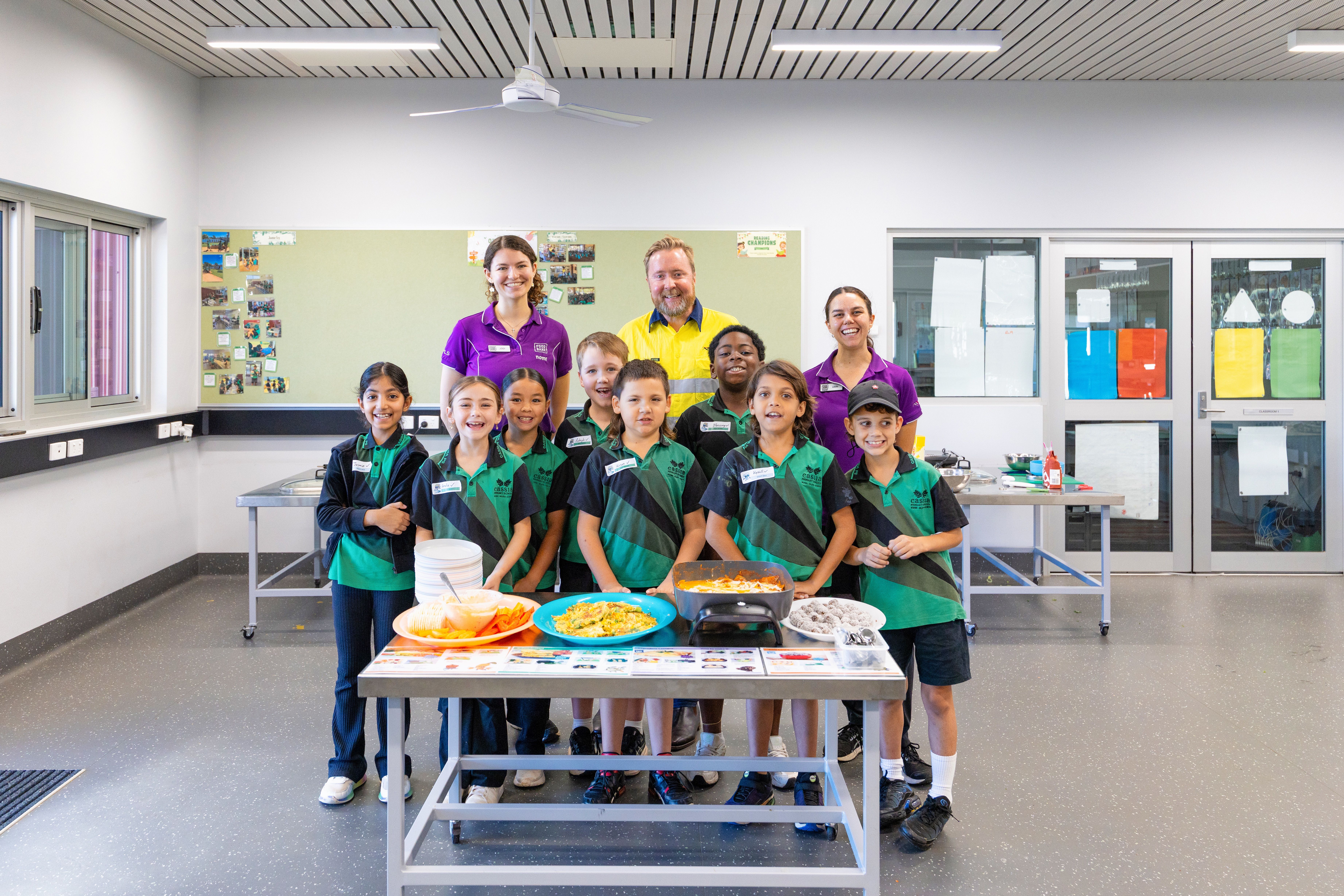 school students smiling with their food and staff standing behind them