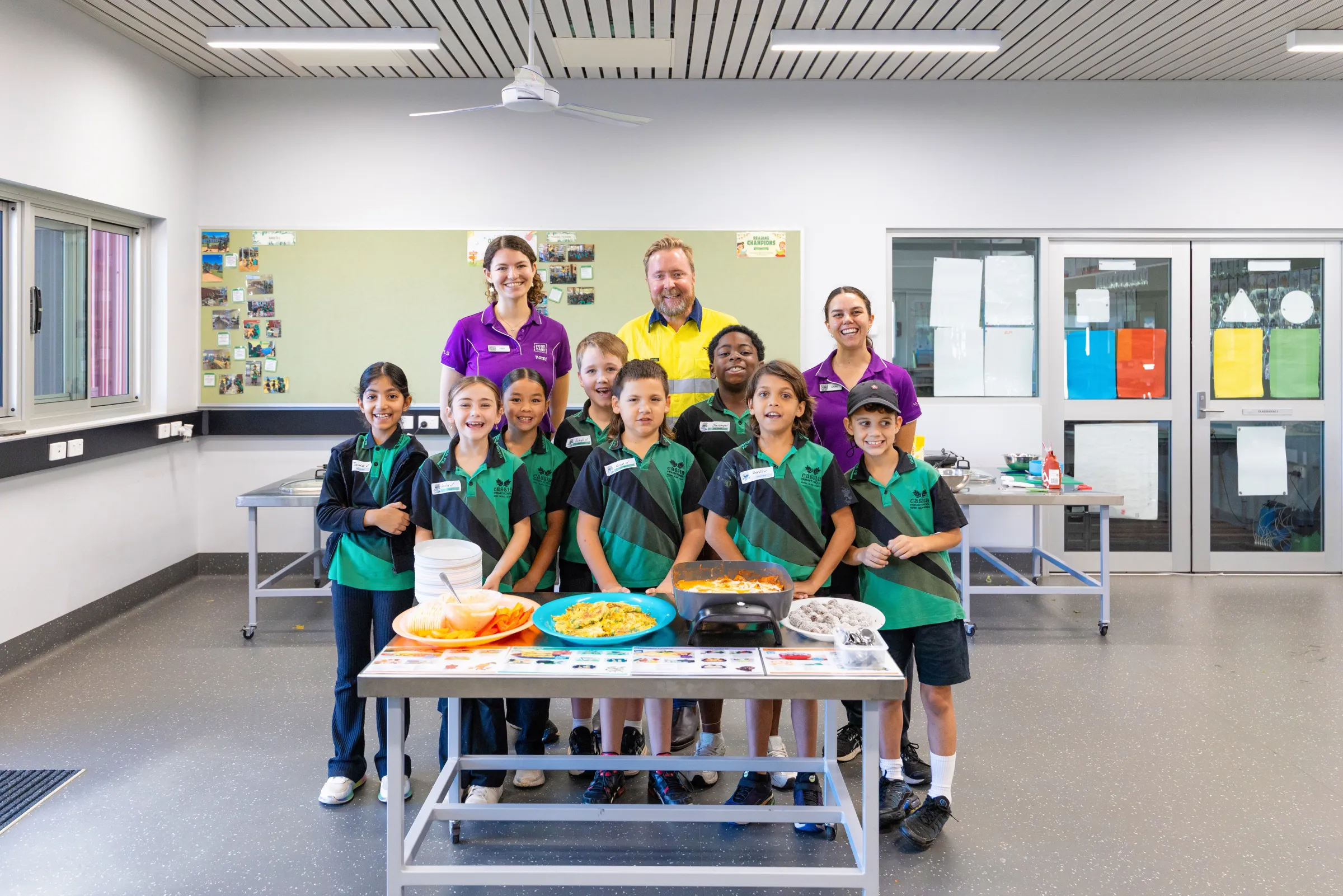 school students smiling with their food and staff standing behind them