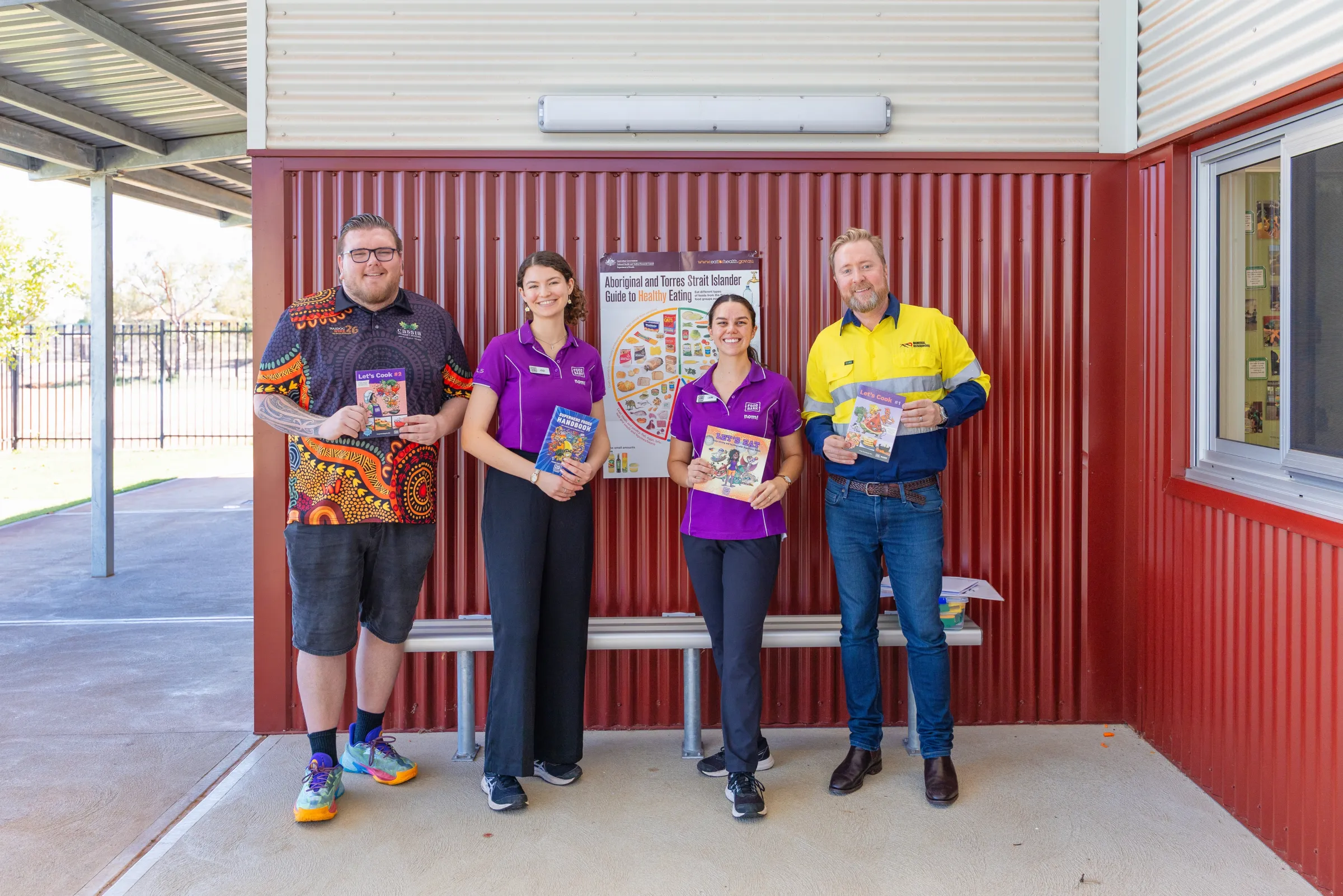 2 men and 2 females standing and smiling at the camera holding the foodbank books