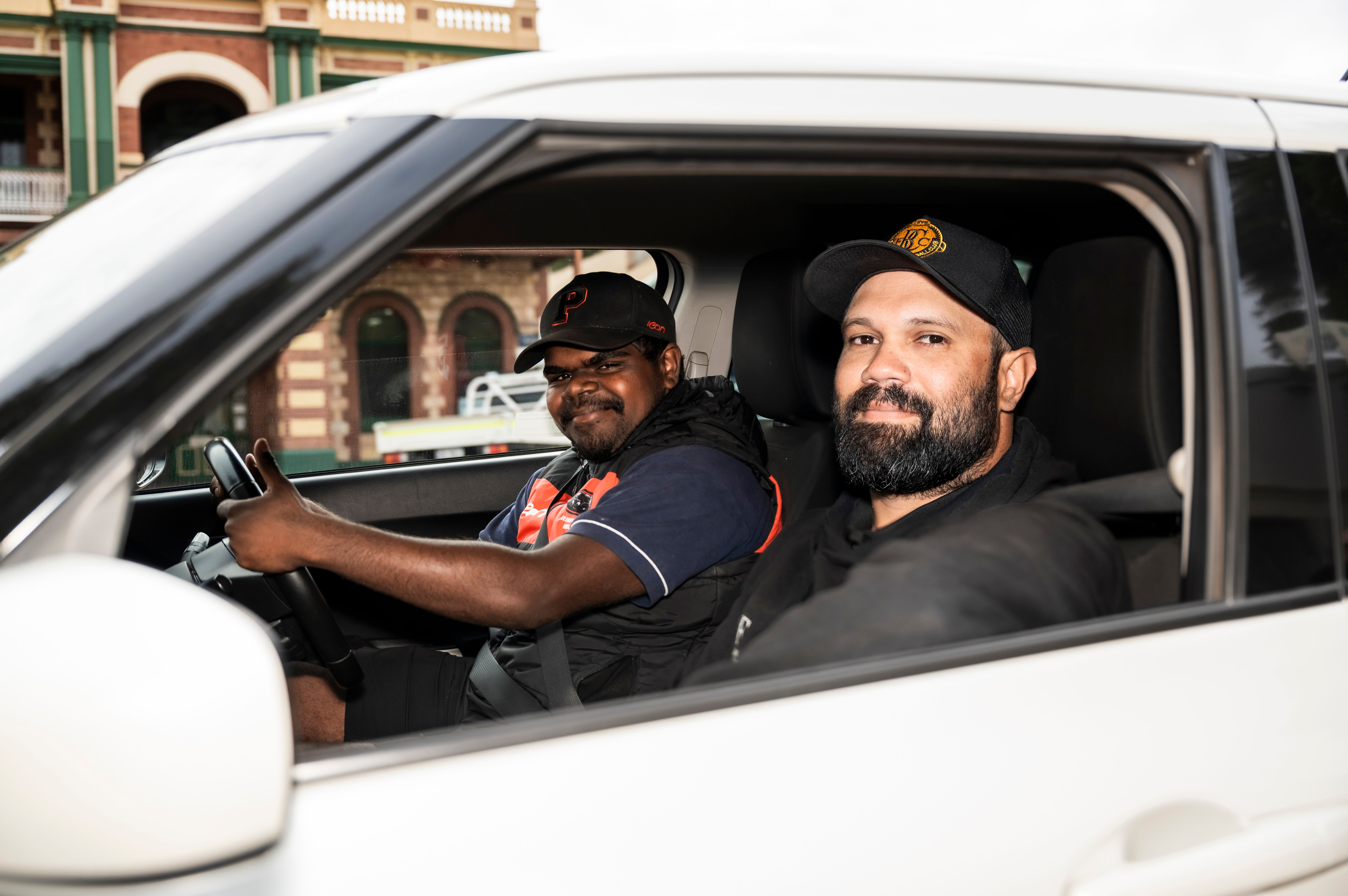 two men sitting inside a car smiling at the camera