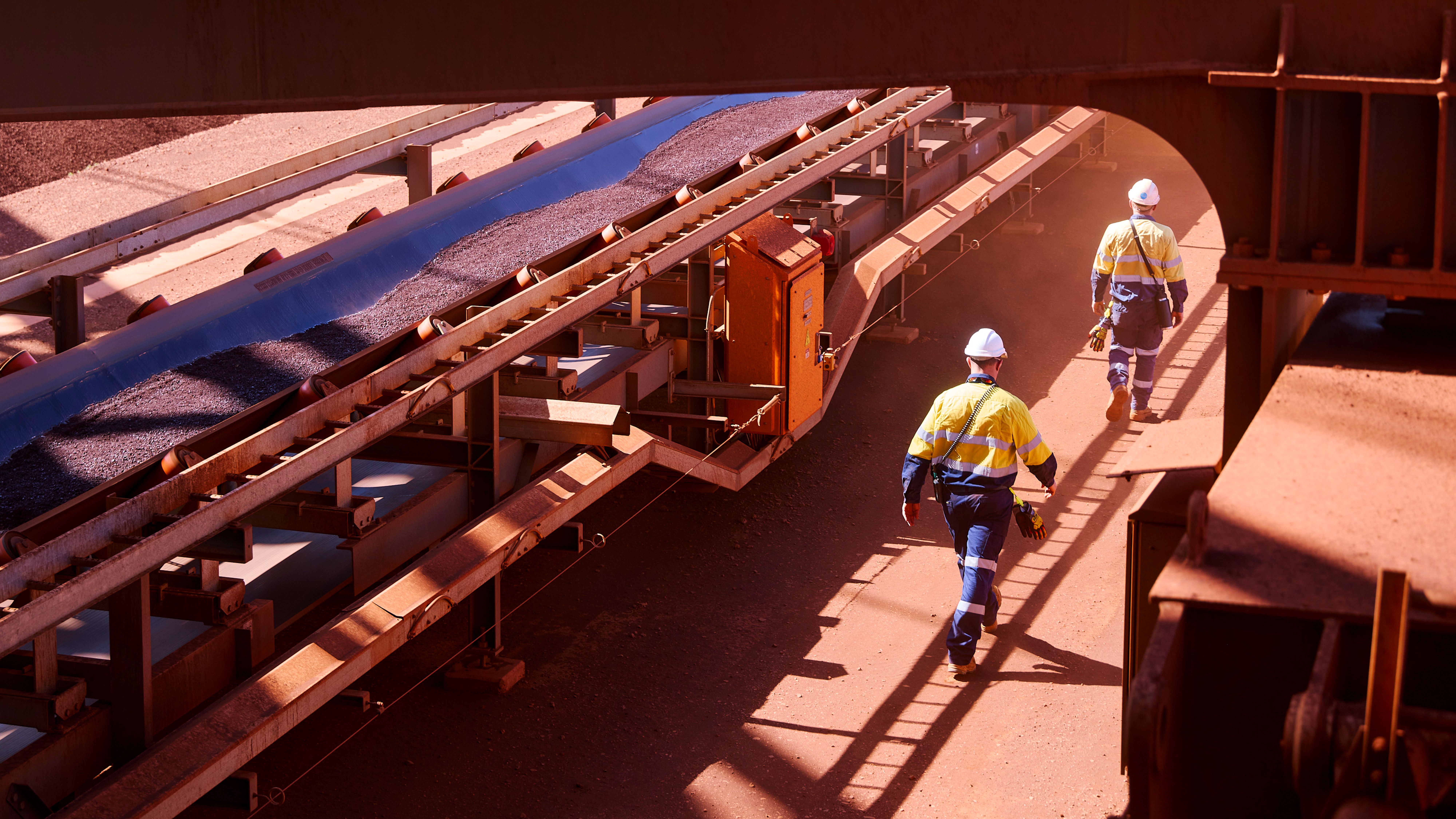 image of two men on site next to conveyor belt of iron ore