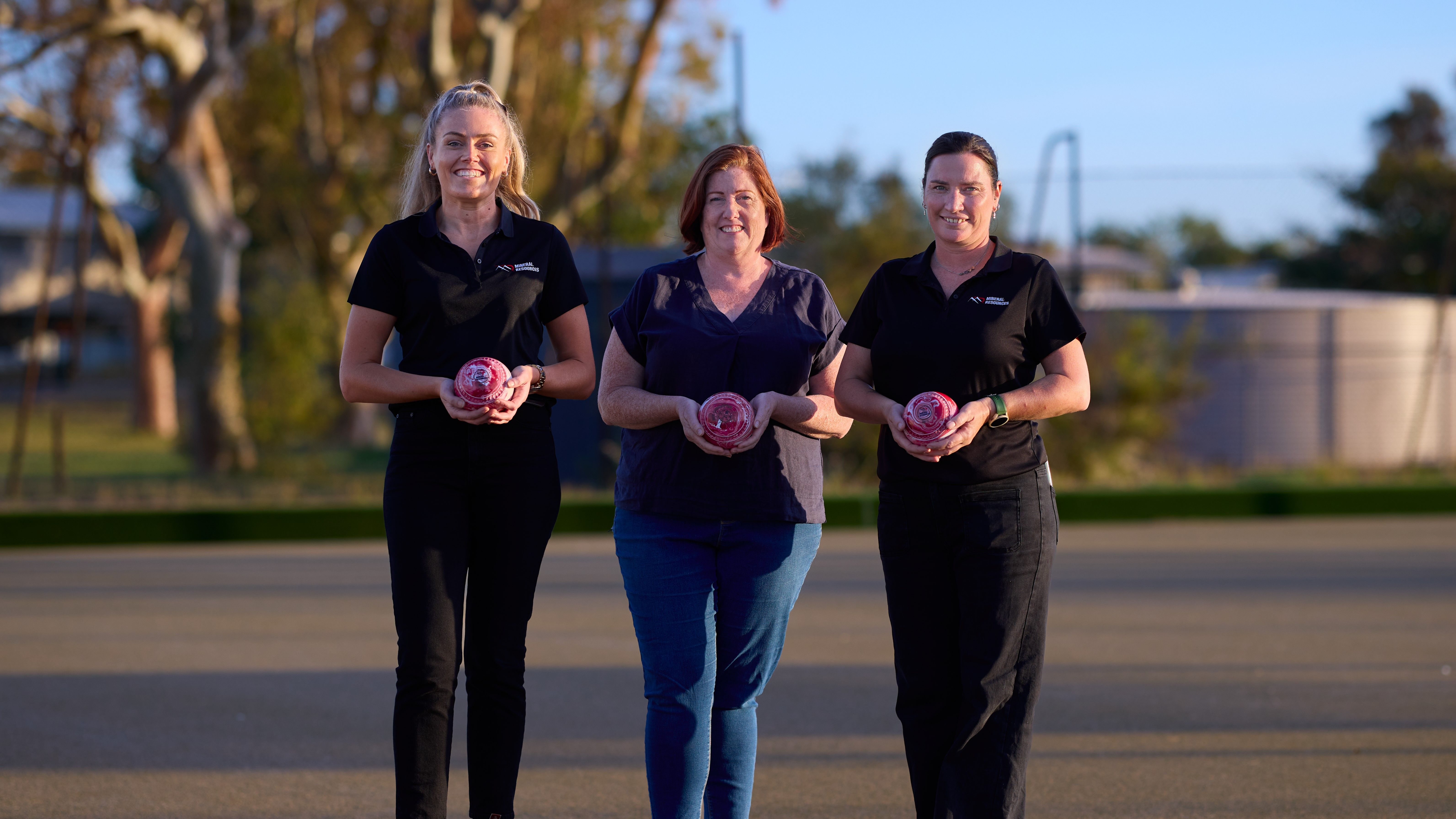 three women standing holding a lawn bowl