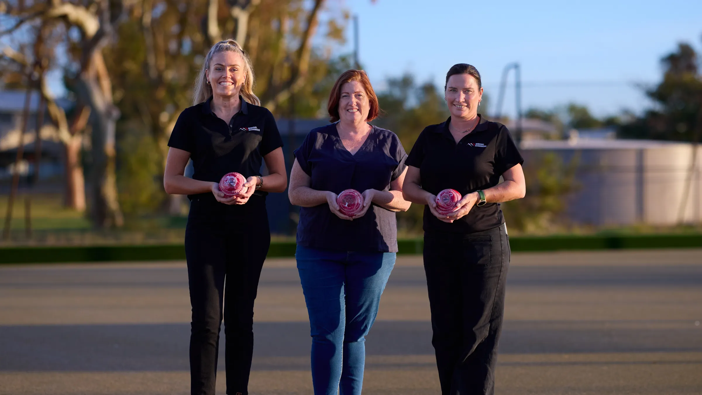 three women standing holding a lawn bowl
