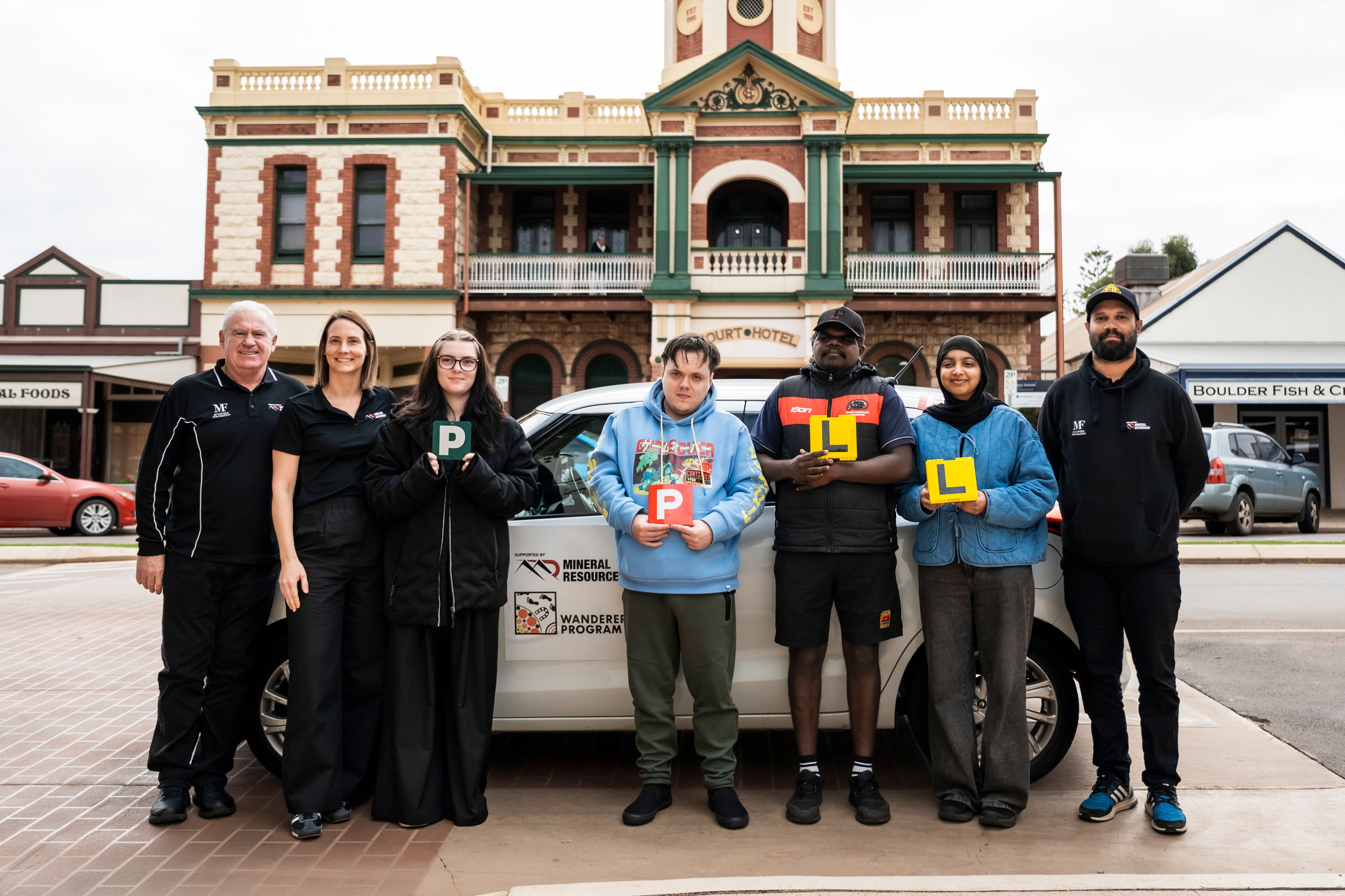 People standing in front of a car holding their P or L plates