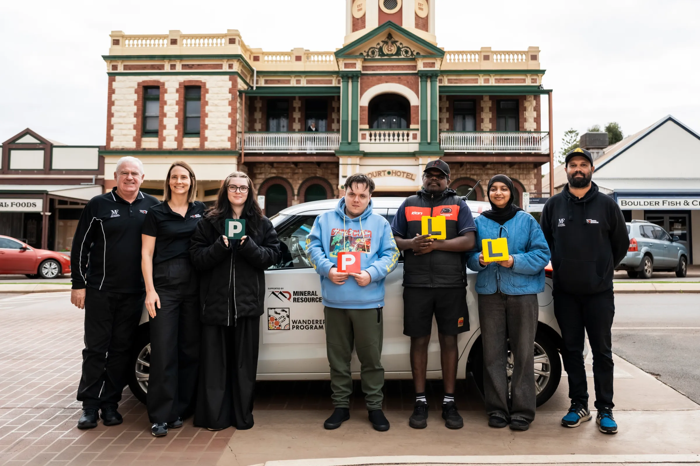 People standing in front of a car holding their P or L plates