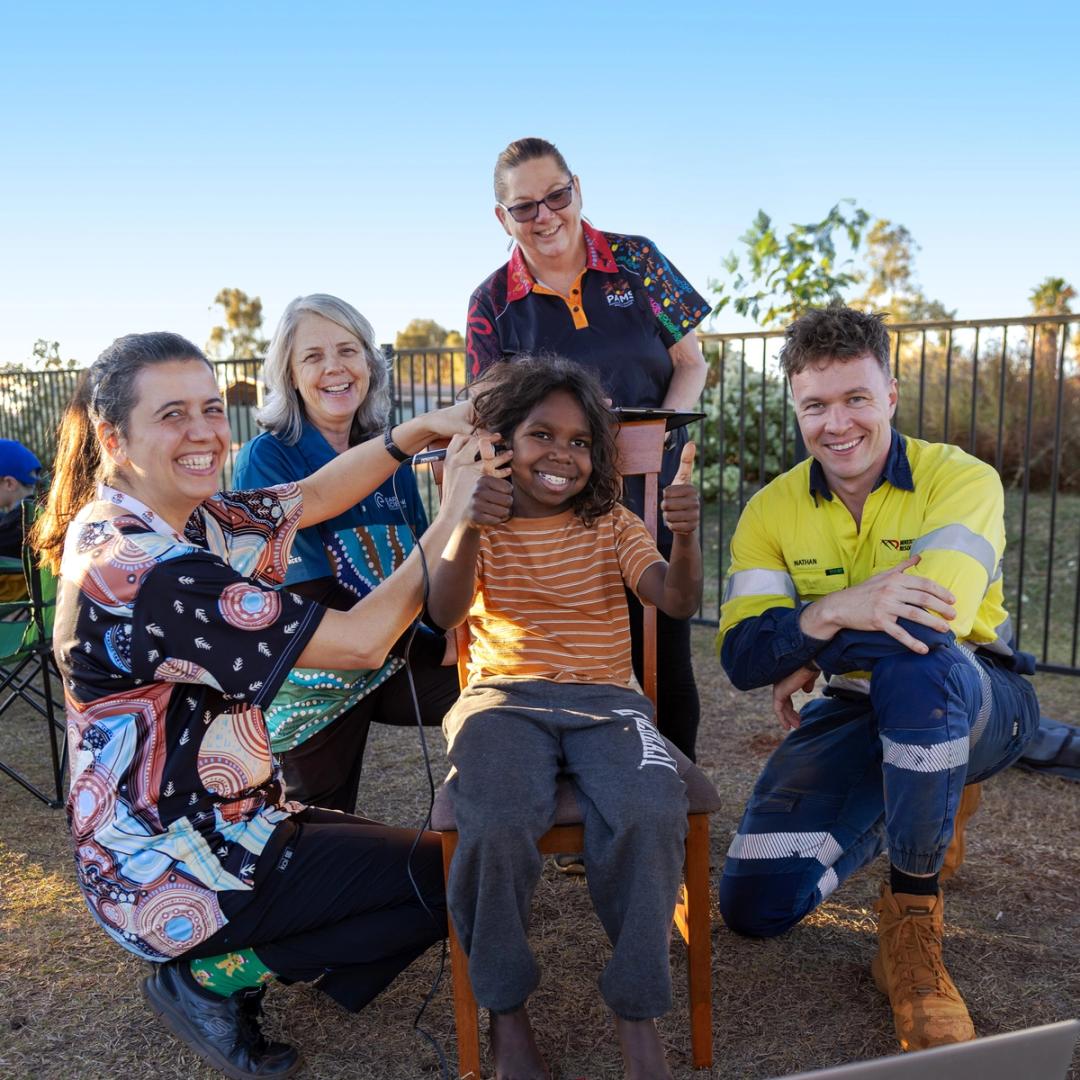 One kid sitting down surrounded by adults
