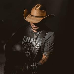 Jason Aldean looking down in a black t-shirt with a cowboy hat covering his eyes 