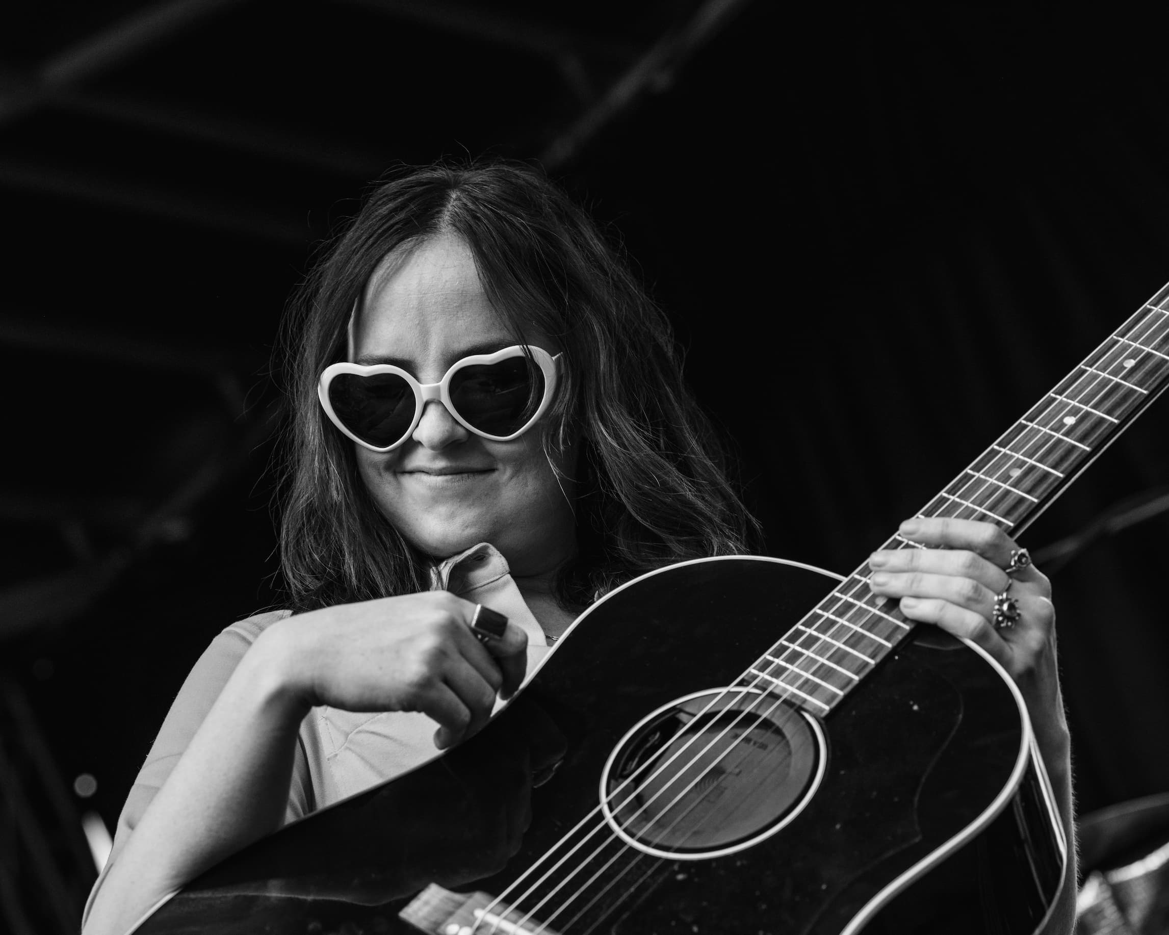 Harper O'Neil in sunglasses adjusting the strap on a guitar that she is holding.