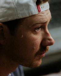 Morgan Wallen looking serious while wearing a backwards ball-cap with a bead of sweat trickling down his head