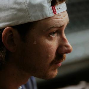 Morgan Wallen looking serious while wearing a backwards ball-cap with a bead of sweat trickling down his head