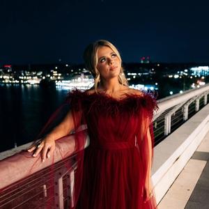 Anne Wilson in a red dress on a balcony