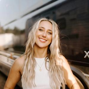 Ashley Cooke smiling in front of her tour-bus