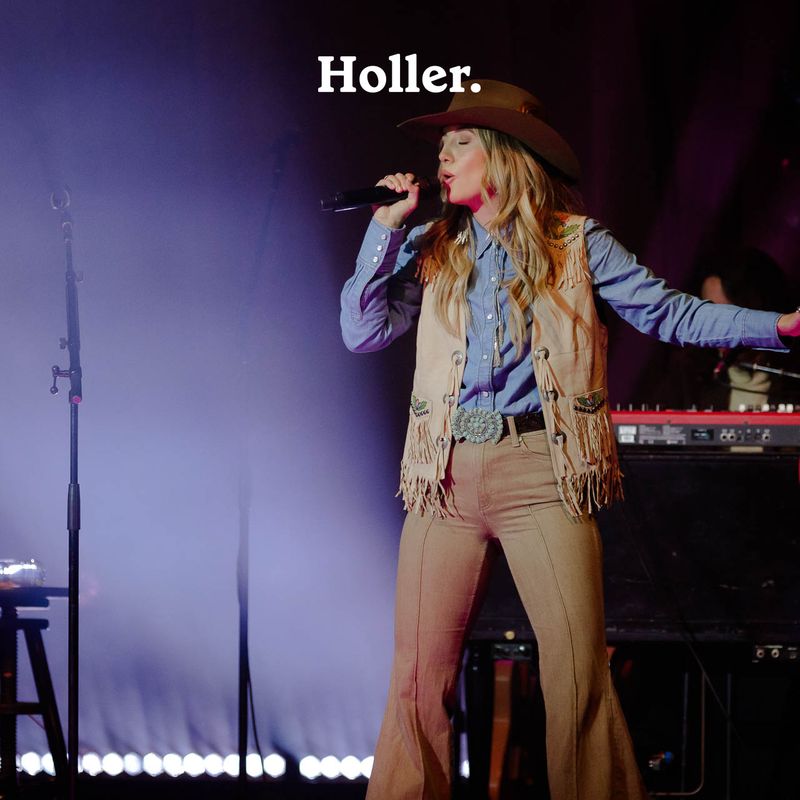 <p>Lainey Wilson sings into a microphone while wearing a beige waistcoat, denim shirt, brown bell bottom jeans and a brown hat, with a keyboard behind her.</p>