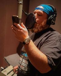Luke Combs recording in a studio with a backwards-cap on