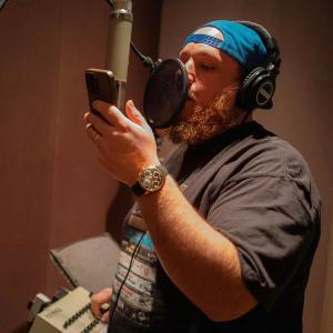 Luke Combs recording in a studio with a backwards-cap on
