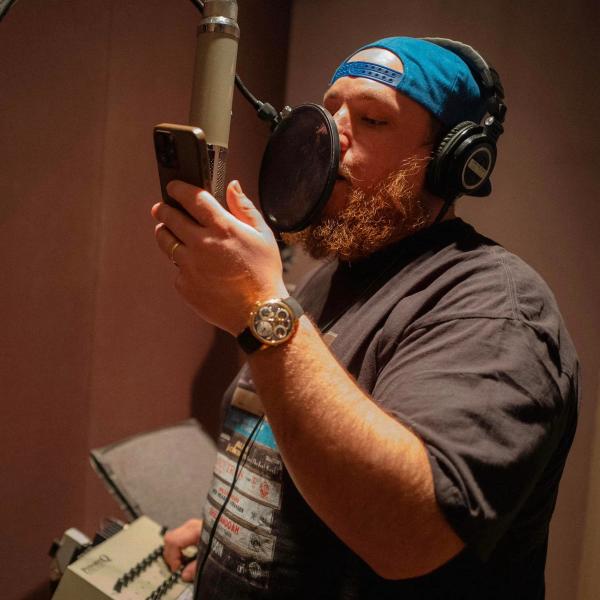 Luke Combs recording in a studio with a backwards-cap on