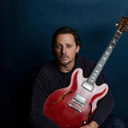 Sturgill Simpson sat holding a red guitar and wearing a black longsleeve top.