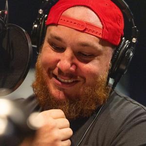 Luke Combs grinning in a red cap