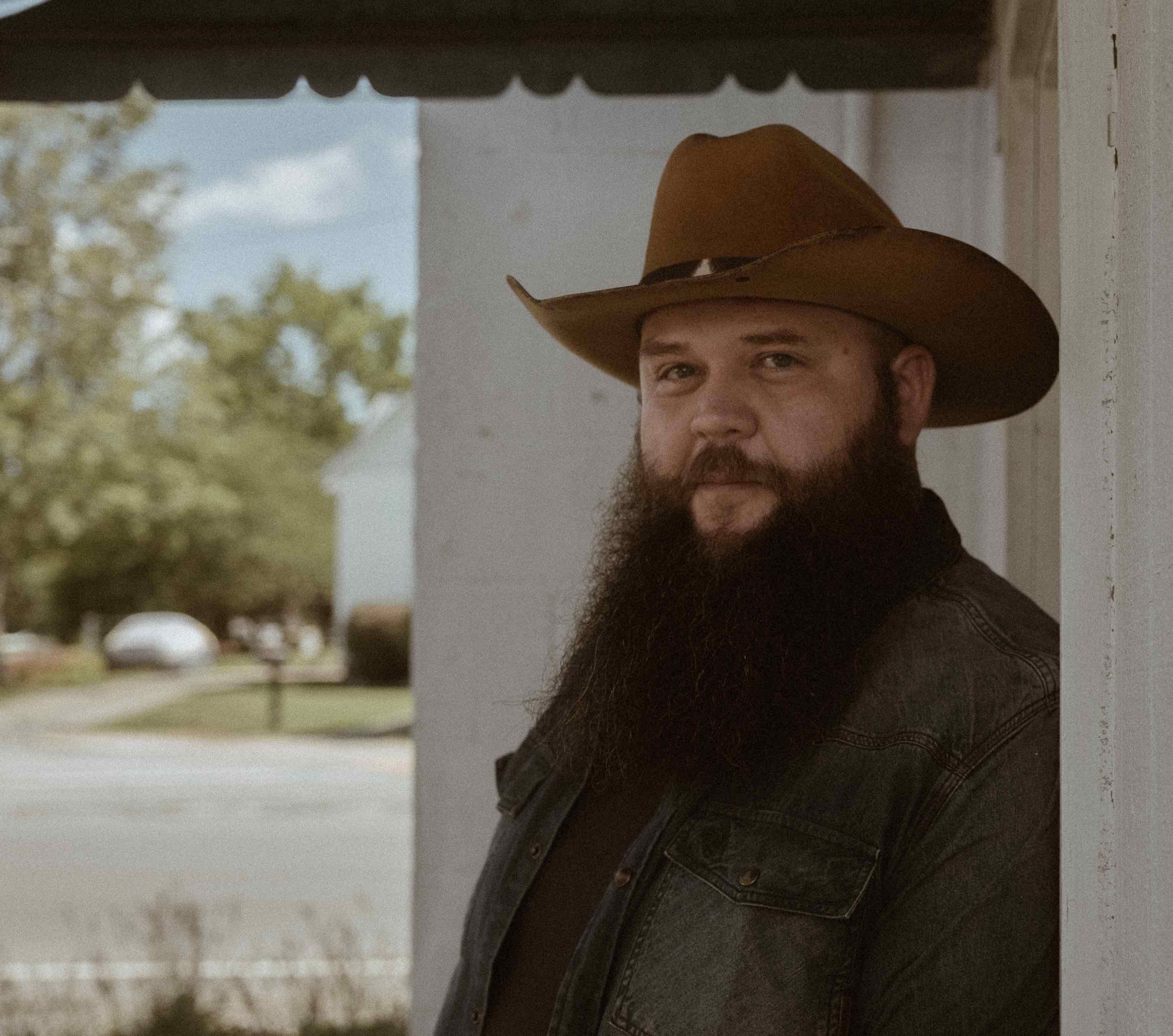 <p>Close-up shot of Larry Fleet in a cowboy hat on the front porch </p>