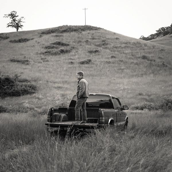 Black and white photo of Josiah standing on a truck bed in a field  