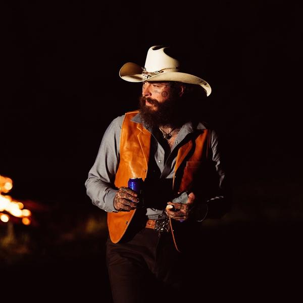 Post Malone with a cowboy hat standing in front of the fire