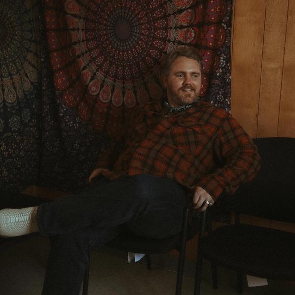 Ernest sitting in a chair against a tapestry