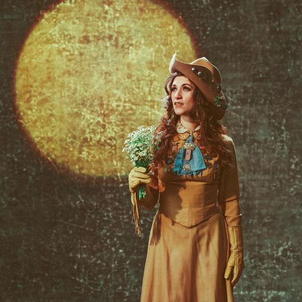 Sierra Ferrell with a hat on and holding flowers in front of a sun-like backdrop