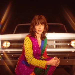 Molly Tuttle sat in front of a car in a multi-coloured outfit