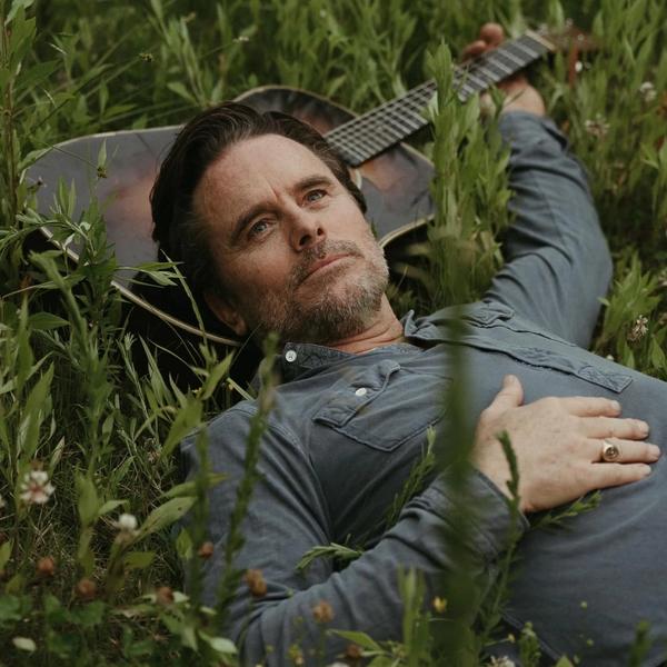 Charles Esten lying in the grass with his guitar